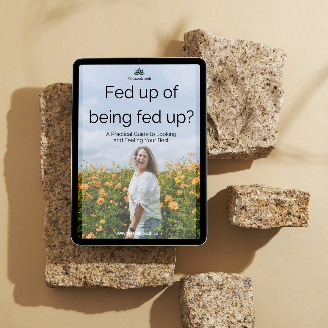 A tablet device lying on rough stone blocks against a warm beige background, displaying a book or guide cover titled "Fed up of being fed up?" with a photo of a woman standing in a field of yellow flowers.