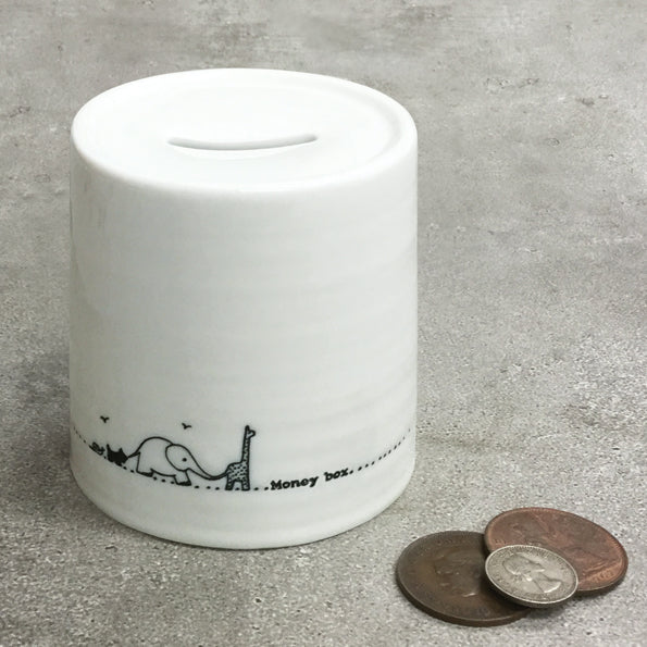 White ceramic money box with black illustrations of an elephant and giraffe, placed on a concrete surface with coins beside it.